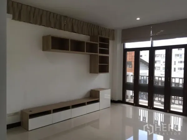 Townhouse for rent in Watthana, Bangkok - Living room with built-in shelving and floor-to-ceiling balcony doors.