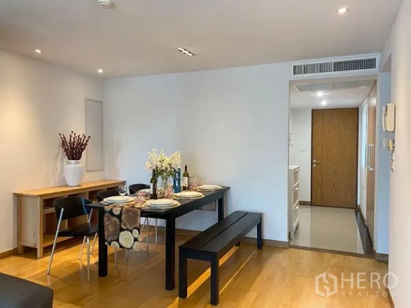 Condominium for sale in Phra Khanong, Bangkok - Dining area with black table and bench seating, recessed lighting, and wooden floors.