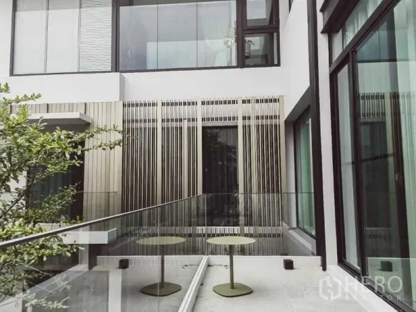 บ้าน ให้เช่า - ทางเชื่อมกระจกพร้อมโต๊ะกลมสองตัว ฉากระแนงและหน้าต่างสูงจรดเพดาน.