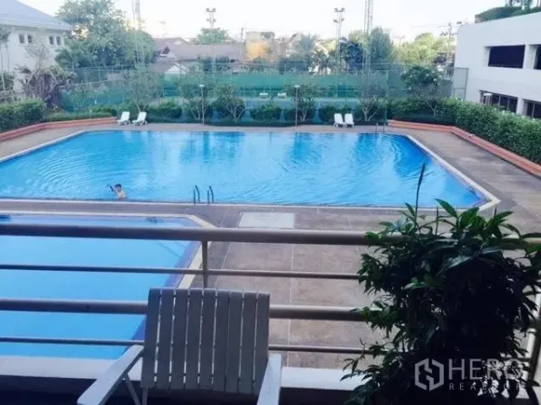 Condominium for rent in Watthana, Bangkok - Balcony view overlooking a large outdoor swimming pool and adjacent tennis courts with loungers.