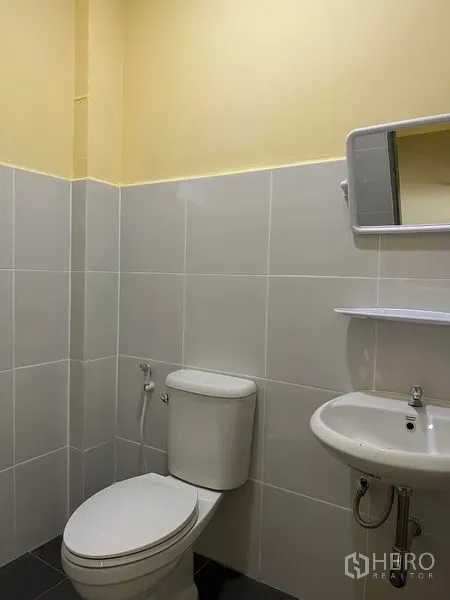 Warehouse for rent or sale in Bang Phli, Samut Prakan - Clean tiled restroom with toilet, sink, mirror and wall shelf inside the warehouse.