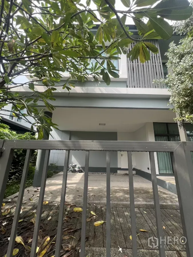 Detached House for sale in Bang Kapi, Bangkok - Two-storey detached house facade with gated driveway and carport shaded by leafy tree.