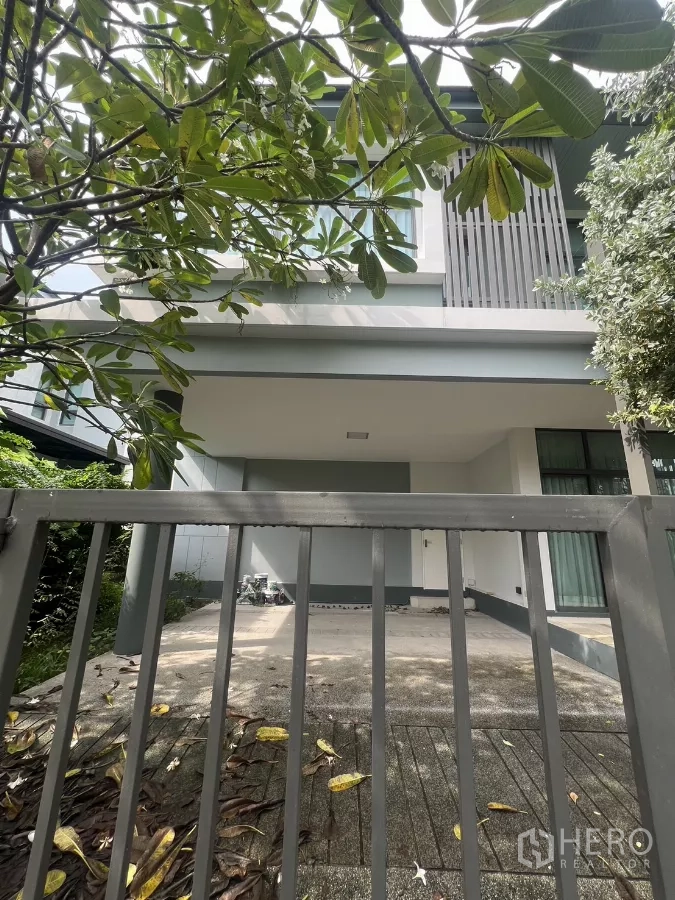 Detached House for sale in Bang Kapi, Bangkok - Two-storey detached house facade with gated driveway and carport shaded by leafy tree.