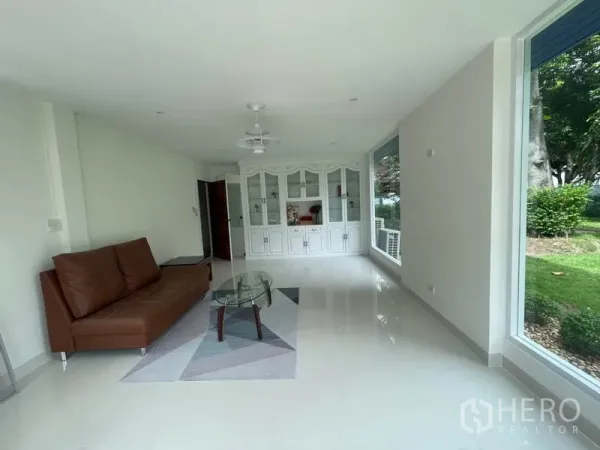 บ้าน ให้เช่าในKhlong Toei, Bangkok - ห้องนั่งเล่นสว่าง กระจกเต็มบาน โซฟาหนังสีน้ำตาล โต๊ะกระจก และตู้บิลท์อินสีขาว มองเห็นสวน