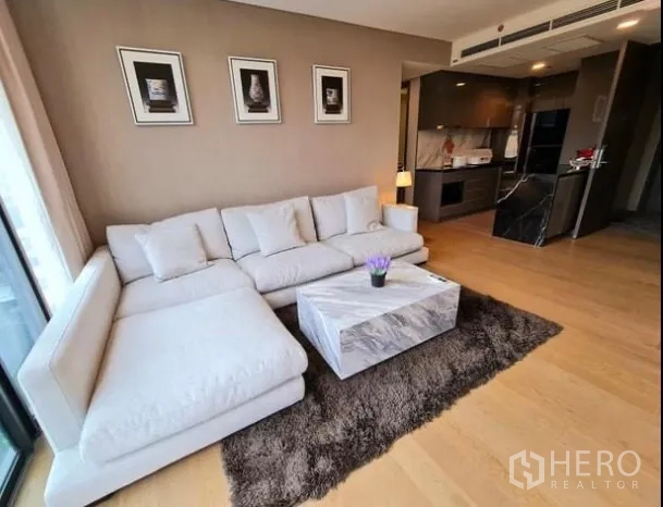 公寓 出租在Khlong Toei, Bangkok - 温馨客厅，白色L形沙发、大理石茶几与长绒地毯，连通开放式厨房