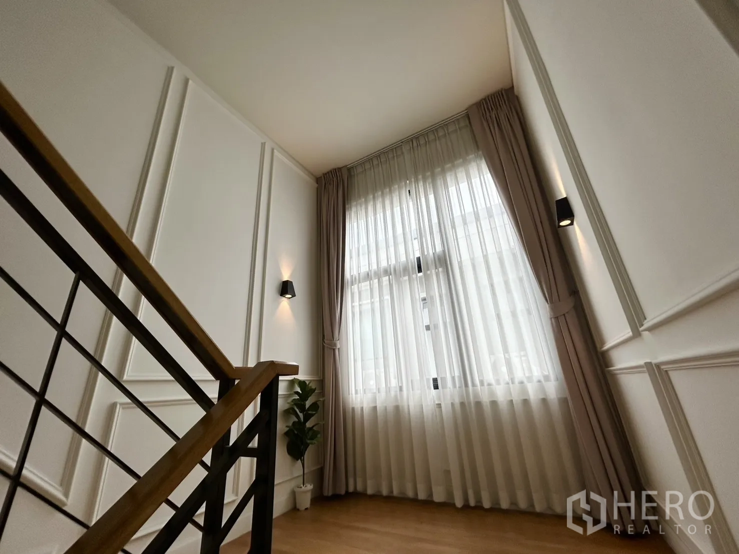 Detached House for rent in Bang Phli, Samut Prakan - Staircase landing with tall curtained window and wall sconces.