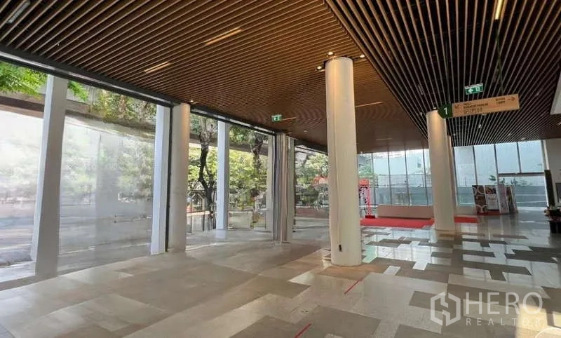 零售空间 出租在Phaya Thai, Bangkok - 开放式大堂型商用区，白色立柱与木格栅天花，三面大玻璃采光，可见街道绿树。