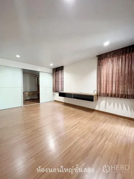 Townhouse for rent or sale in Don Mueang, Bangkok - Master bedroom with wood floors, curtains and sliding door to dressing area.