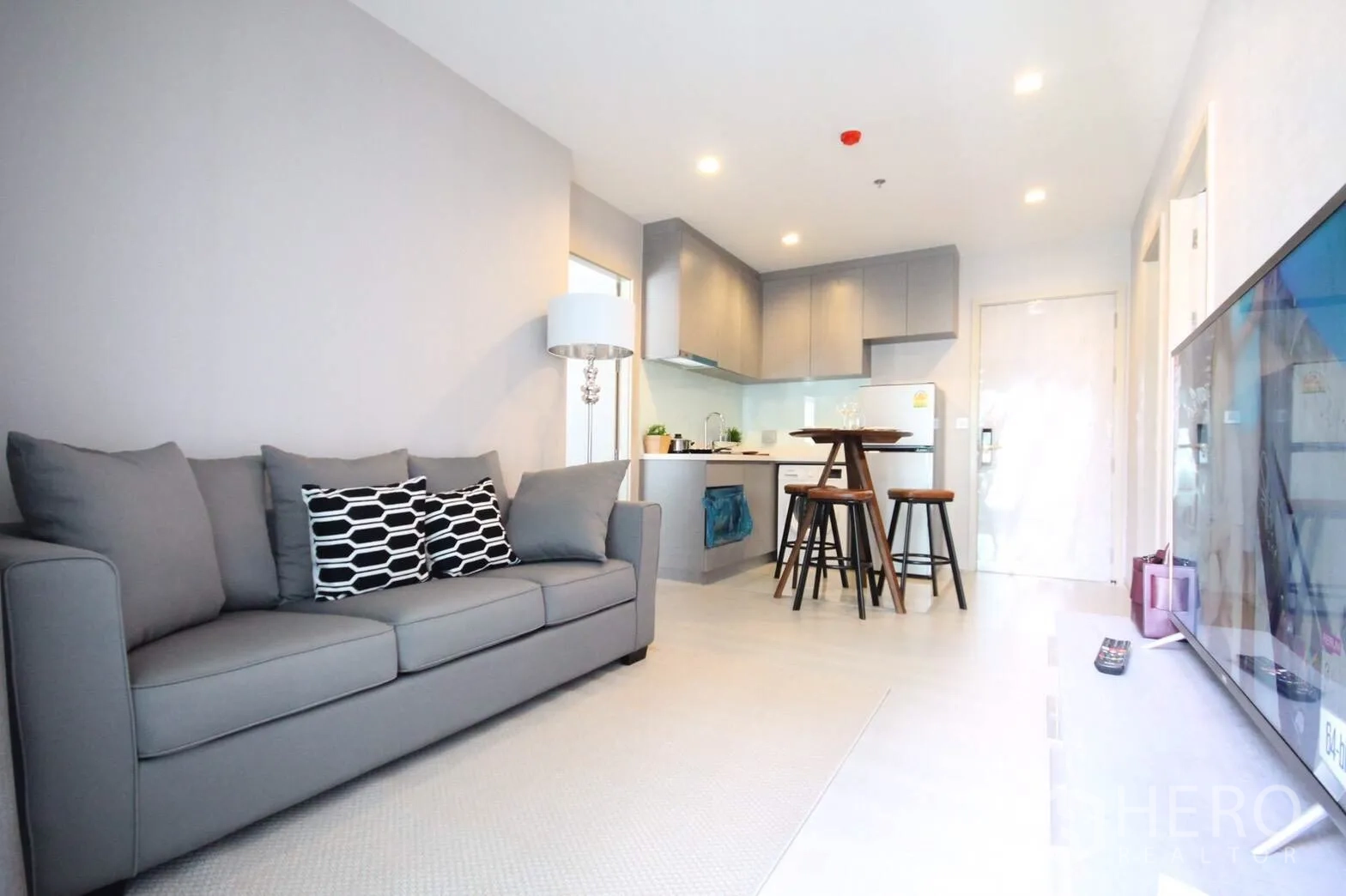 Condominium for rent in Khlong Toei, Bangkok - View from living area to kitchen with grey cabinets, breakfast bar and stools beside a cosy sofa.