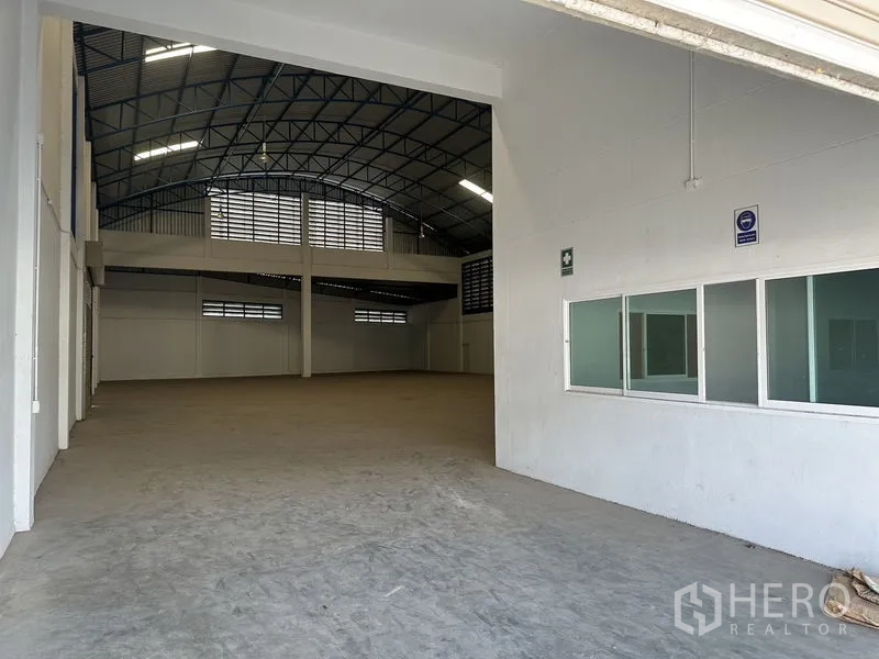 Factory for rent in Bang Bo, Samut Prakan - Entrance to the warehouse showing spacious interior and adjacent office windows beneath a high steel roof.