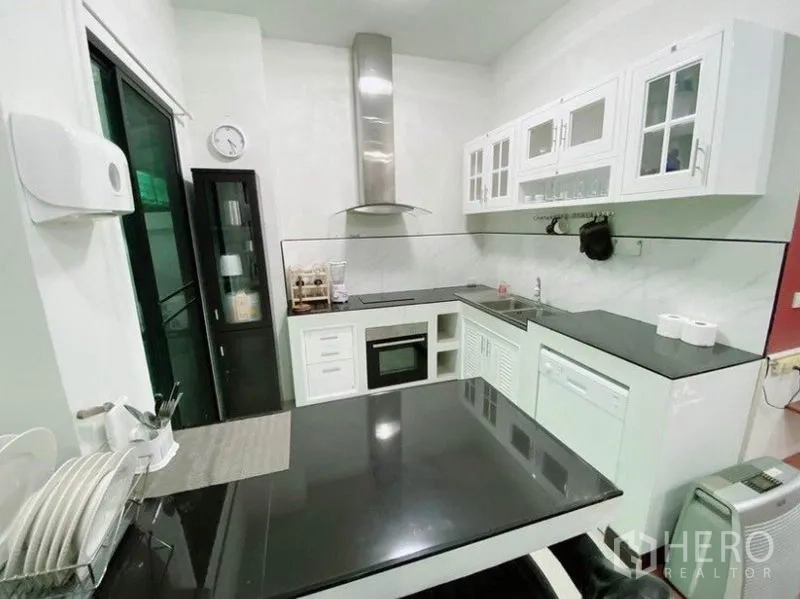 Townhouse for rent in Wang Thonglang, Bangkok - Modern white kitchen with black countertops, oven, cooktop, and stainless-steel hood.