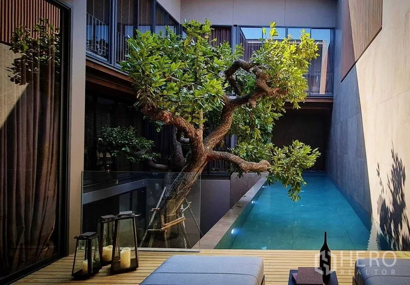 独立式住宅 出售在Lat Phrao, Bangkok - 庭院泳池配绿树与玻璃护栏，被现代立面环绕。