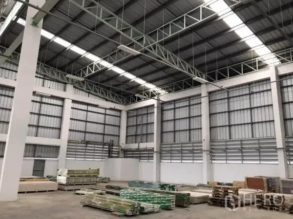 Warehouse for rent in Sai Noi, Nonthaburi - High-clear storage hall with ventilated walls and stacked building materials on the floor.