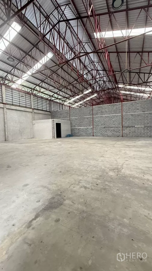 Warehouse for rent in Min Buri, Bangkok - Wide open warehouse space showing skylights, steel beams and a block wall partition.