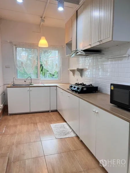 Detached House for rent - Light kitchen with white cabinets, wood countertops, gas hob, hood and window.