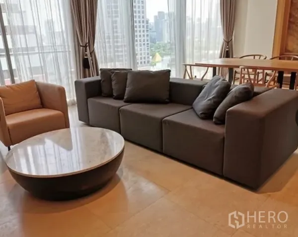 公寓 出租在Bang Rak, Bangkok - 现代客厅，灰色模块沙发、单人椅与圆形大理石茶几临窗而置。