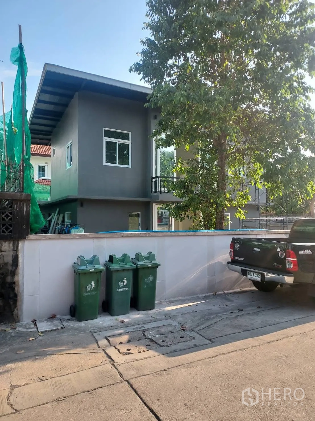 Detached House for rent in Watthana, Bangkok - Front street view of the detached house behind a low wall with a mature tree.