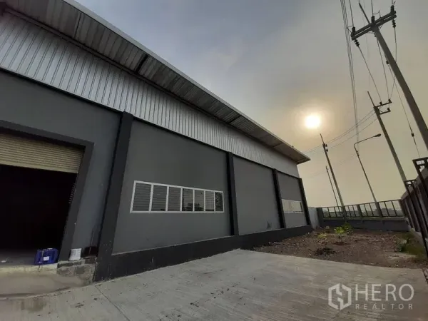 คลังสินค้า ให้เช่าในLam Luk Ka, Pathum Thani - ด้านหน้าโกดังสีเทา ลานคอนกรีต ประตูม้วน และกำแพงรอบโครงการ