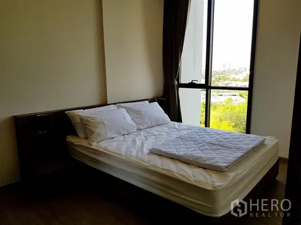 Condominium for rent in Watthana, Bangkok - Bedroom with large window, double bed, and leafy city outlook.