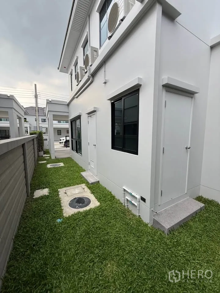 Detached House for rent in Don Mueang, Bangkok - Rear side of the house with lawn walkway and utility doors.