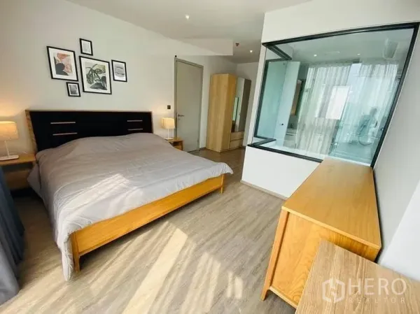 公寓 出租在Watthana, Bangkok - 主卧空间宽敞，木质家具，玻璃隔断可见浴室。