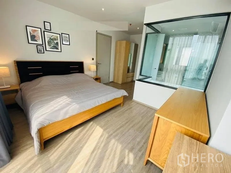 公寓 出租在Watthana, Bangkok - 主卧空间宽敞，木质家具，玻璃隔断可见浴室。