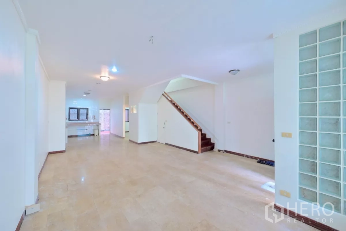 Townhouse for sale in Watthana, Bangkok - Bright open living area with neutral flooring and side staircase.