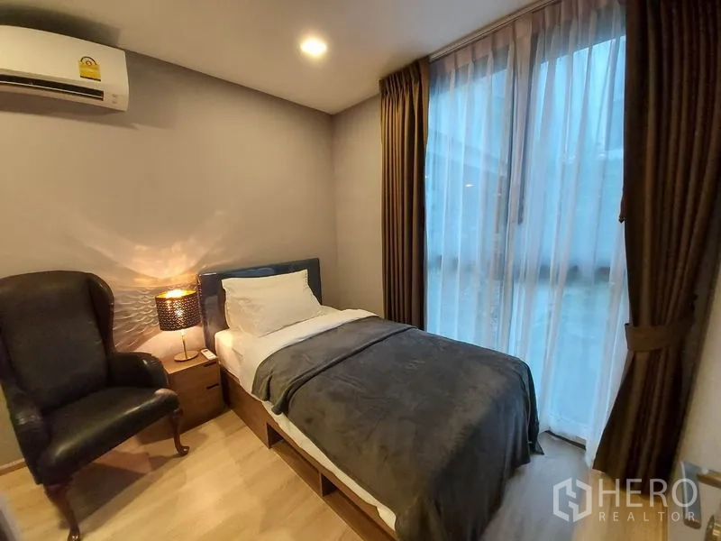 คอนโด ให้เช่าหรือขายในWatthana, Bangkok - ห้องนอนเล็กเตียงเดี่ยว เก้าอี้อาร์มแชร์ และหน้าต่างสูงจรดเพดานพร้อมม่าน