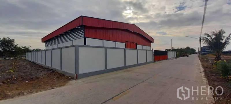 货栈 出租或出售在Khlong Luang, Pathum Thani - 转角视角，沿混凝土道路的围墙仓库用地，道路旁有棕榈树。