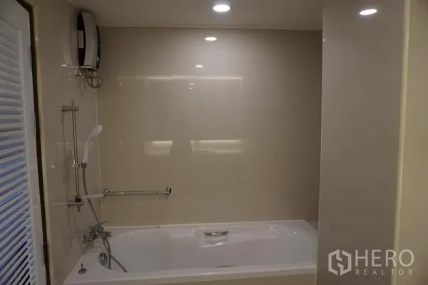 Condominium for rent in Watthana, Bangkok - Bathroom with beige tiles, bathtub and handheld shower set.