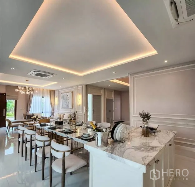 Detached House for sale in Bang Phli, Samut Prakan - Open-plan kitchen with marble island adjoining a long dining table and cove lighting.