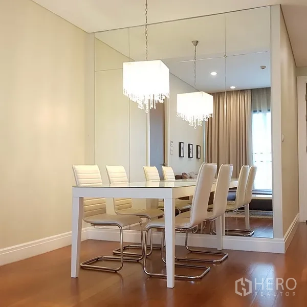 公寓 出租在Khlong Toei, Bangkok - 餐区设白色餐桌与座椅，镜面墙与水晶吊灯增强空间感。
