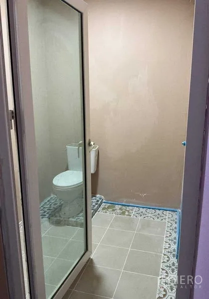 Warehouse for rent in Sai Noi, Nonthaburi - Simple bathroom with a toilet behind a glass door and patterned floor tiles.