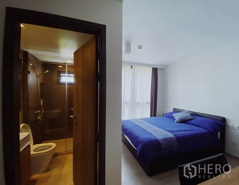 คอนโด ให้เช่าในPathum Wan, Bangkok - ห้องนอนใหญ่ผ้าปูสีน้ำเงิน พร้อมห้องน้ำในตัวด้านหลังประตูไม้