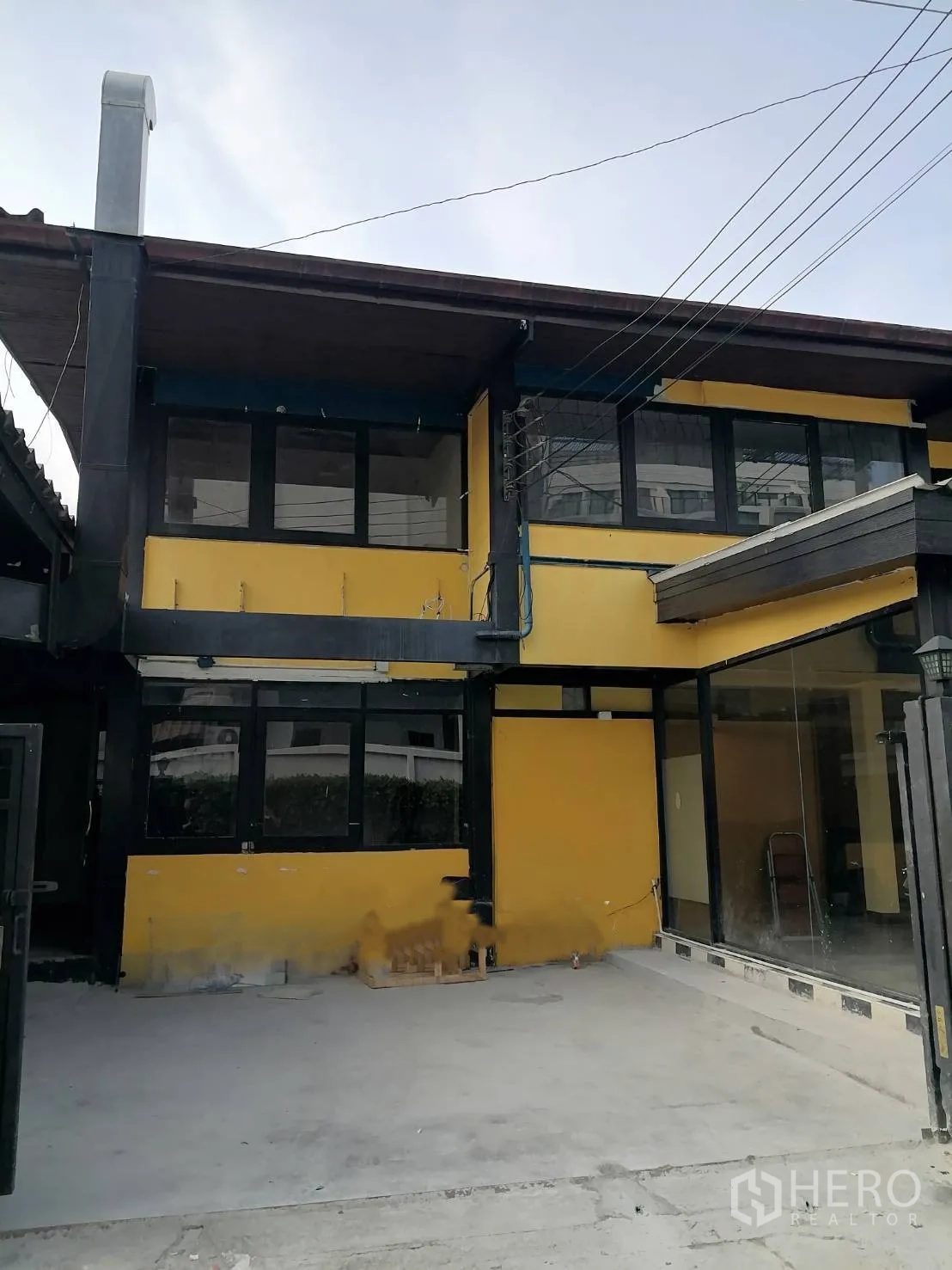 Detached House for rent in Watthana, Bangkok - Two-story yellow detached house with black trim, large windows, and a concrete front courtyard.