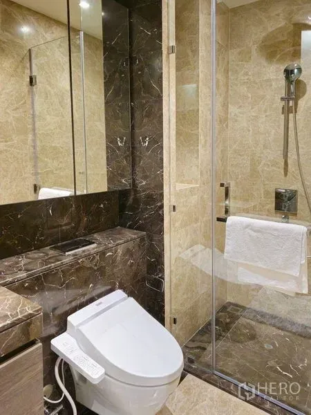 Condominium for rent or sale in Pathum Wan, Bangkok - Marble bathroom featuring a bidet toilet, mirrored cabinets, and a glass-enclosed shower.