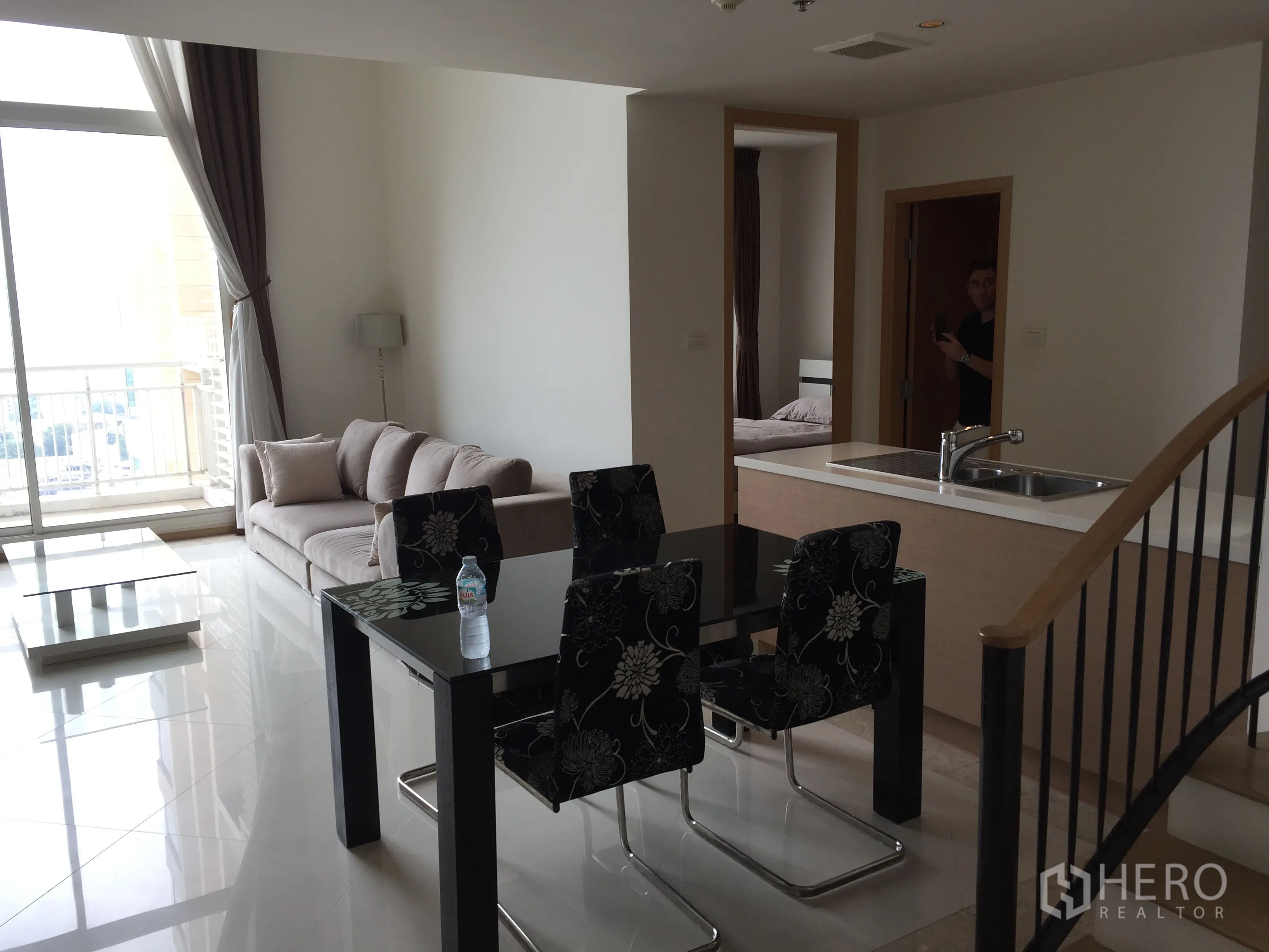 Condominium for rent in Sathon, Bangkok - Open living and dining area with floor-to-ceiling window and balcony access beside the kitchen and staircase.