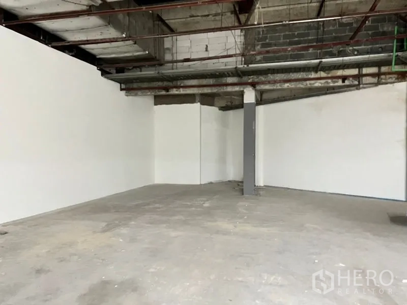 零售空间 出租在Khlong Toei, Bangkok - 白色围墙、大型零售区与中央立柱，天花为开放式。