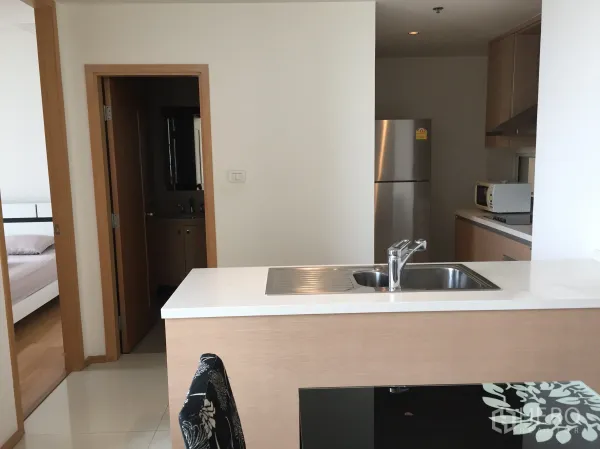 Condominium for rent in Sathon, Bangkok - Modern kitchen with island sink, stone countertop, stainless refrigerator and built-in cabinets leading toward bedrooms and bathroom.