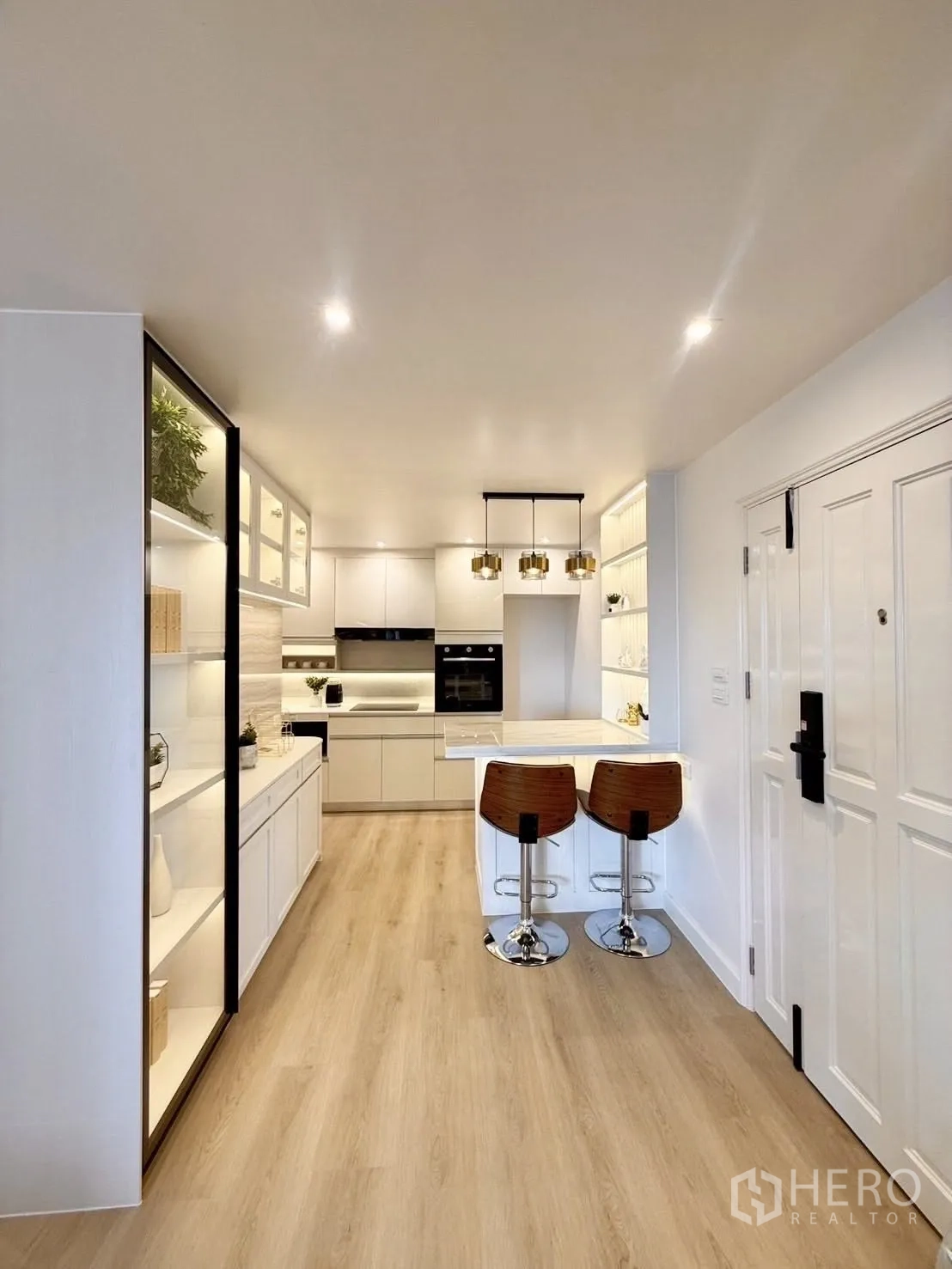 Condominium for rent or sale in Yan Nawa, Bangkok - Open-plan white kitchen with a marble island breakfast bar, pendant lights and wood flooring.