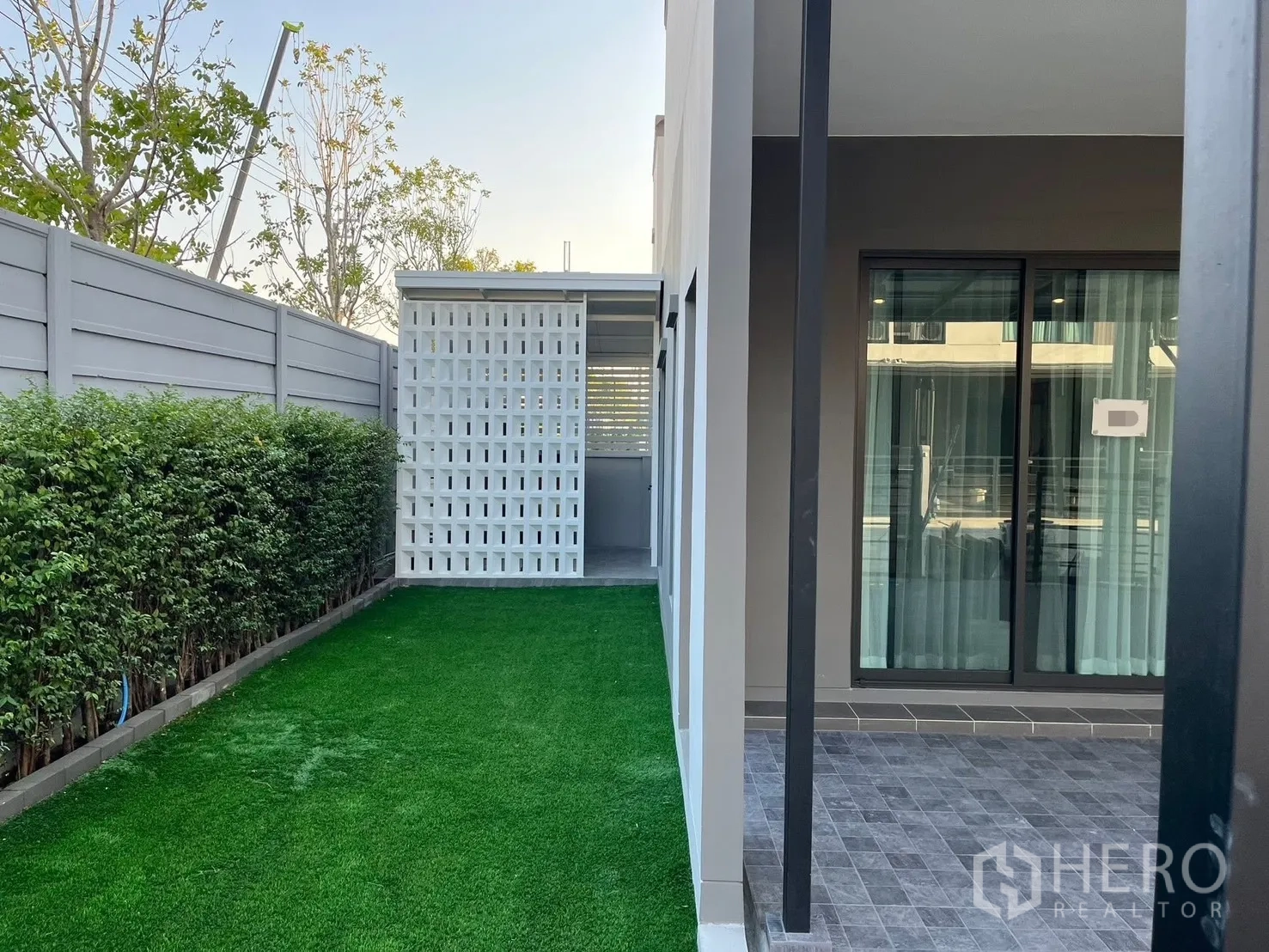 联排别墅 出租在Bang Phli, Samut Prakan - 联排别墅侧院，人工草坪、绿篱和带顶露台，旁有推拉玻璃门。