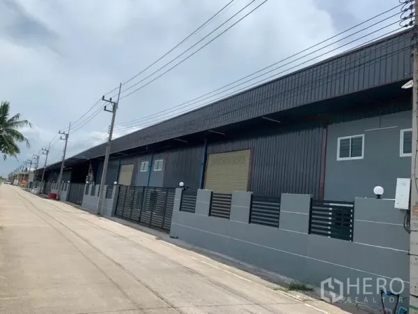 Factory for rent in Khlong Luang, Pathum Thani - Long row of industrial warehouse units along power lines and a concrete road in Khlong Luang.