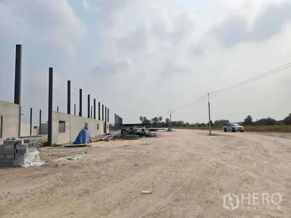 Warehouse for sale in Ban Bueng, Chon Buri - Wide gravel yard and access road beside a warehouse construction site with utility poles and open fields in Ban Bueng.