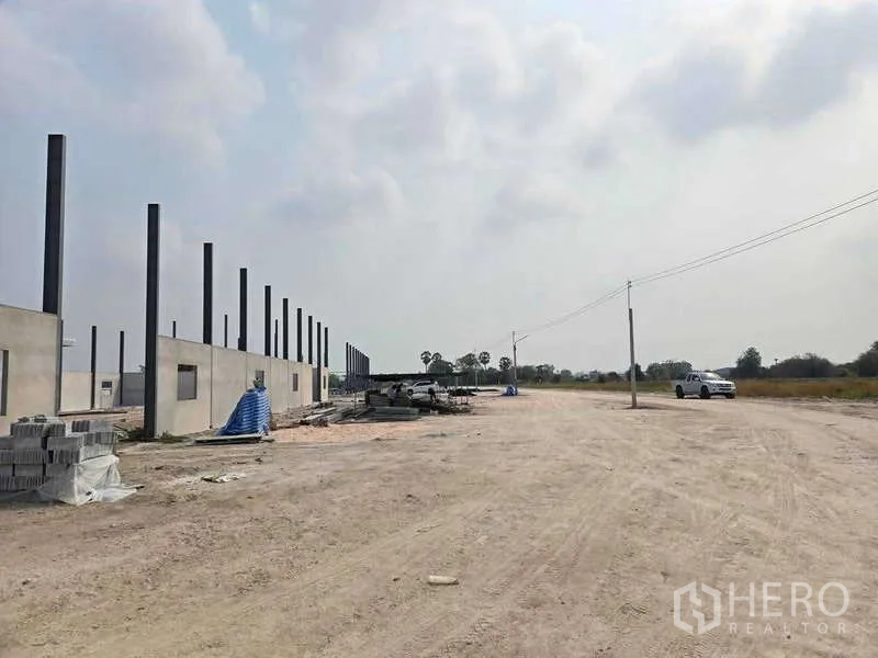 Warehouse for sale in Ban Bueng, Chon Buri - Wide gravel yard and access road beside a warehouse construction site with utility poles and open fields in Ban Bueng.