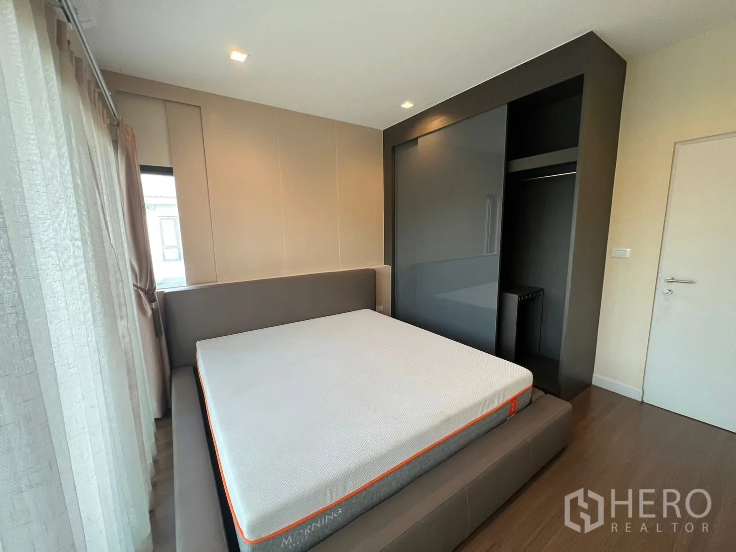 Detached House for rent in Bang Phli, Samut Prakan - Bedroom with built-in dark wardrobe, platform bed, and corner windows with curtains.