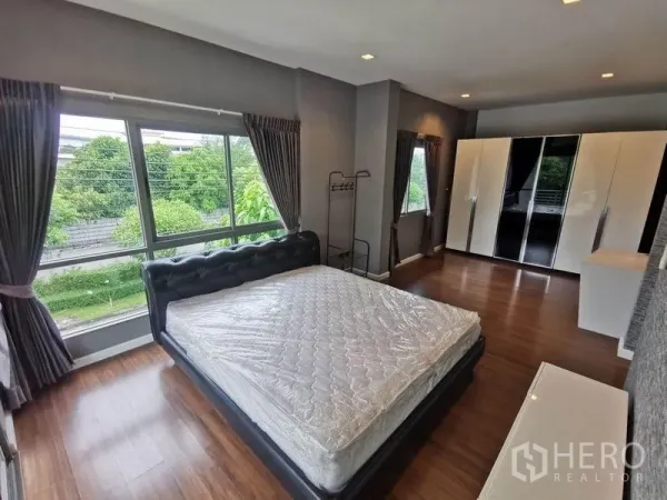 Detached House for rent in Prawet, Bangkok - Spacious master bedroom with large windows, double bed and wardrobes overlooking greenery.