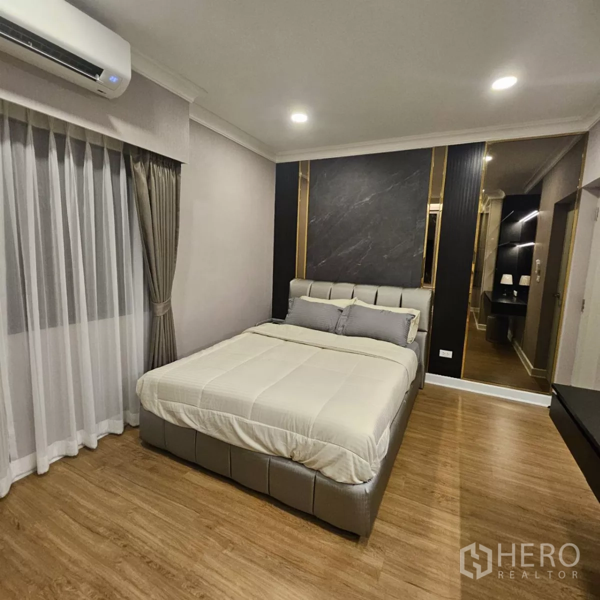 Detached House for rent in Bang Phli, Samut Prakan - Bedroom with upholstered bed, wood floors, drapes and a dark feature wall with gold trim and vanity.
