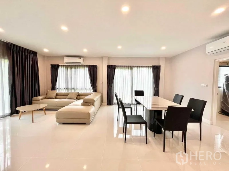 Detached House for rent in Don Mueang, Bangkok - Dining table for six next to a large sectional sofa in a light-filled lounge.