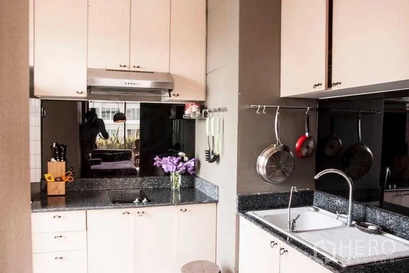 Condominium for rent in Watthana, Bangkok - Fitted kitchen with light cabinetry, black granite countertops, mirrored splashback and hanging cookware.