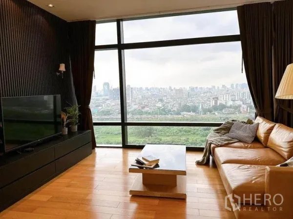 Condominium for rent in Ratchathewi, Bangkok - Lounge with leather sofa facing a full-height window showcasing Bangkok cityscape and greenery.
